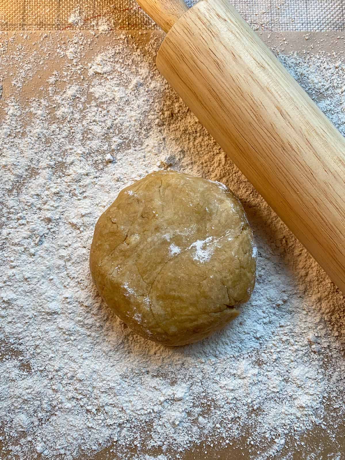 Disk of dough on a floured surface, with a rolling pin nearby.