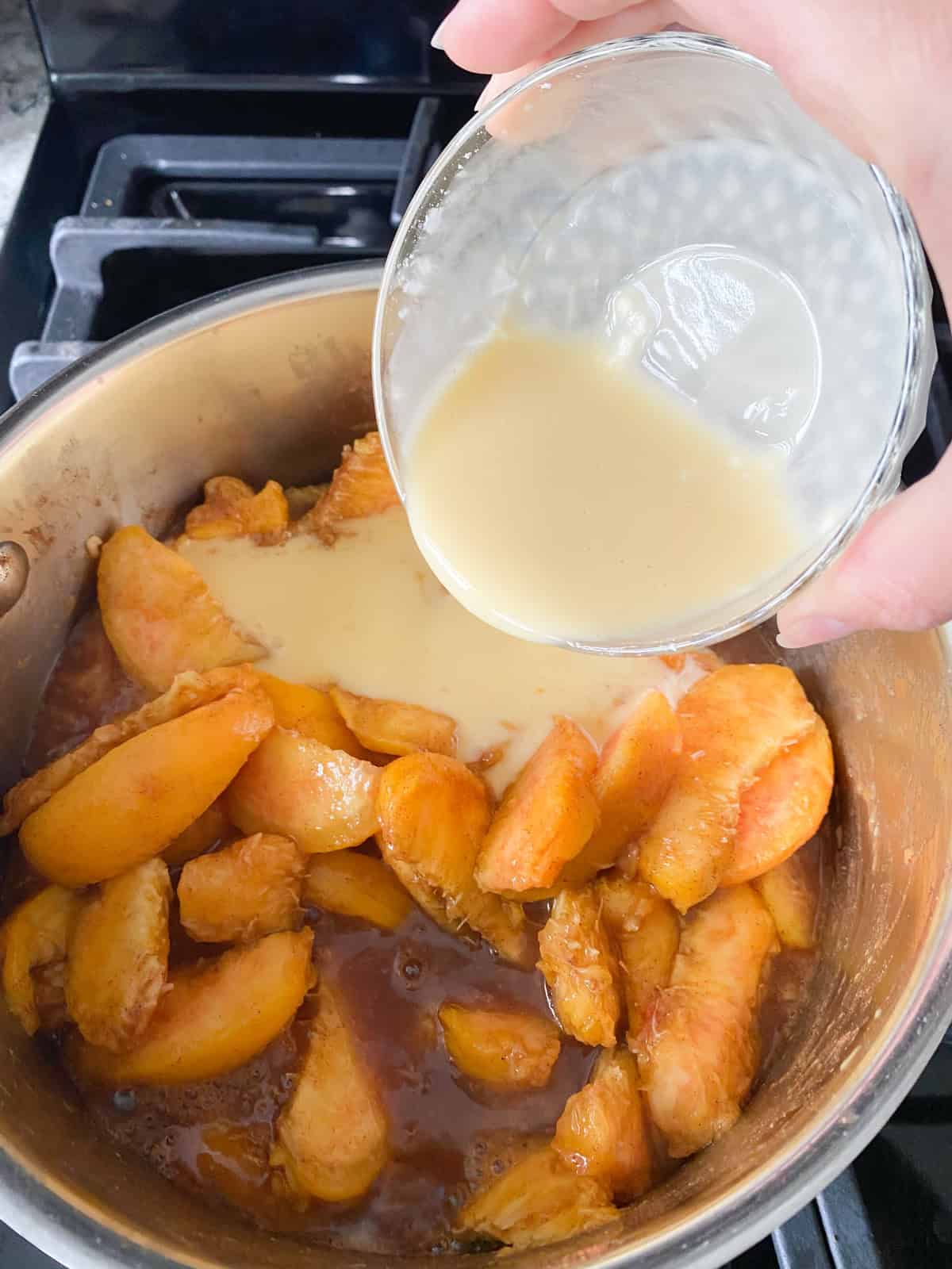Peach nectar being poured into cooking peaches.