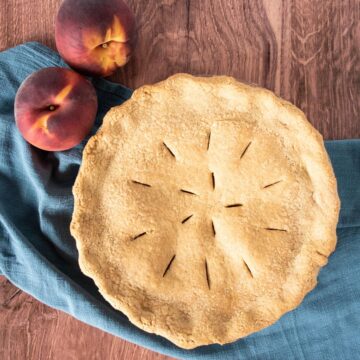 Overhead shot of a whole pie, with fresh peaches beside it.