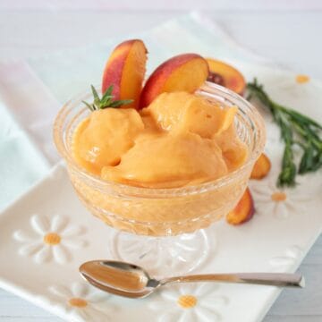 Glass dish with three scoops of peach sorbet; garnished with peach slices and fresh tarragon.