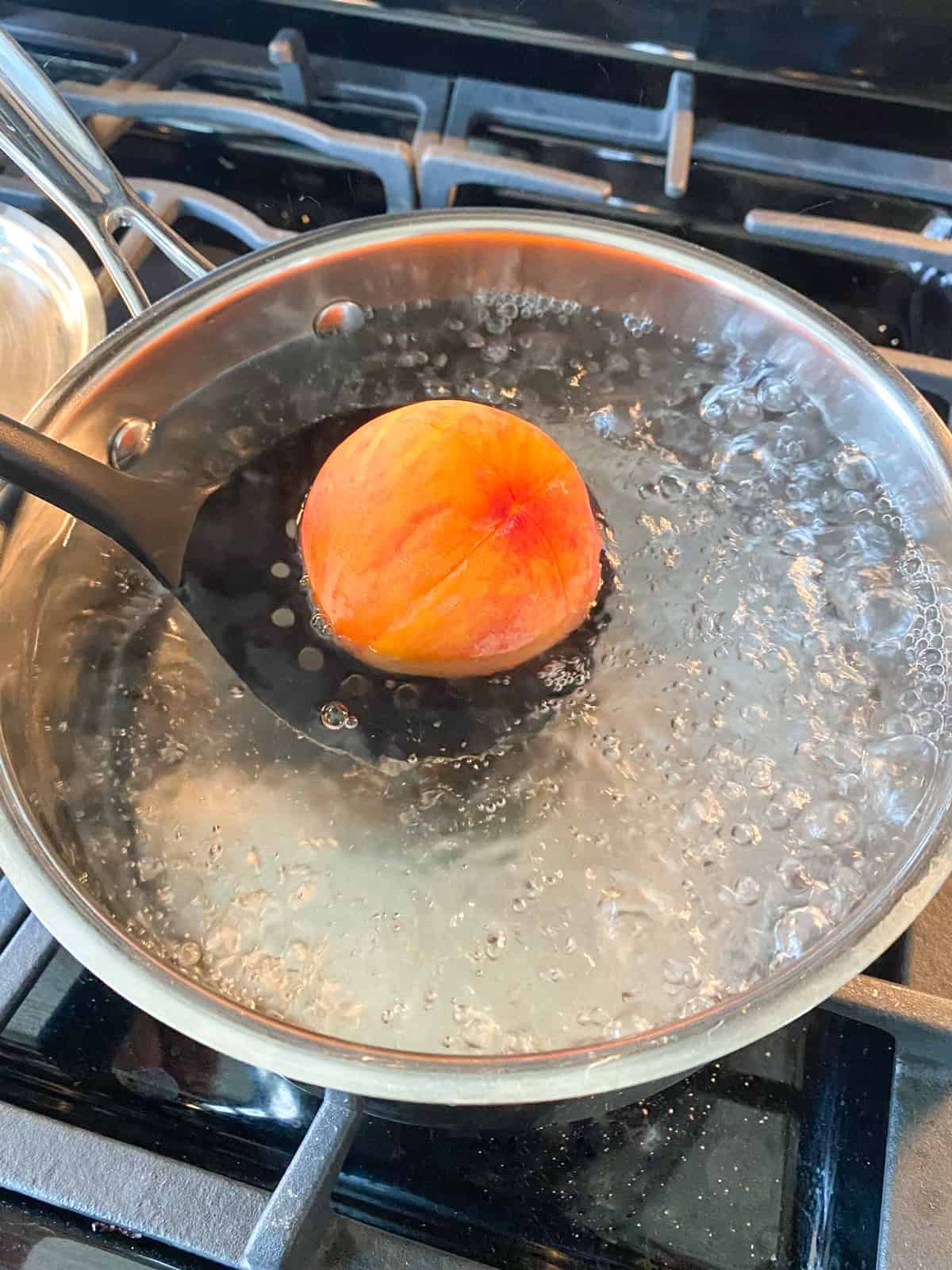 Fresh peach being lowered into boiling water.