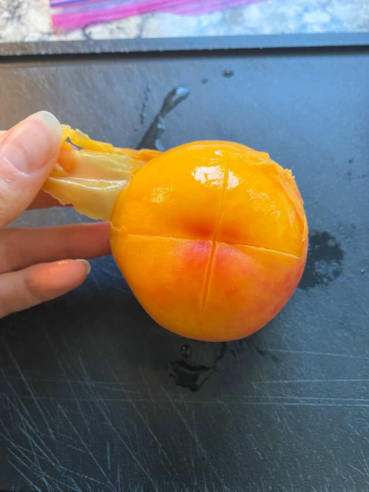 A blanched peach, being peeled, on a cutting board.