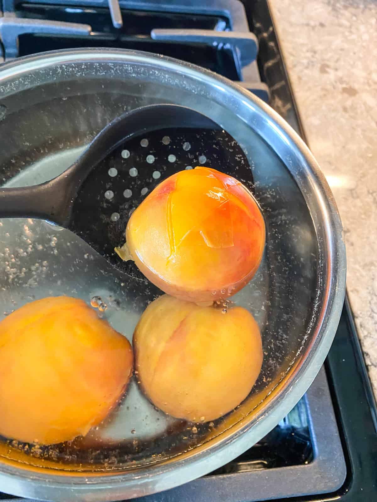 Blanched peach, being removed from boiling pot.