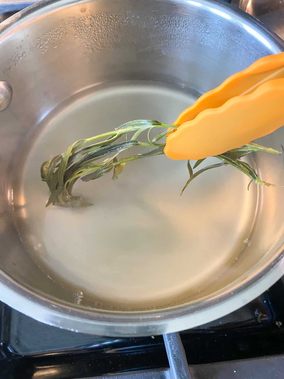 Fresh tarragon being removed from liquid.