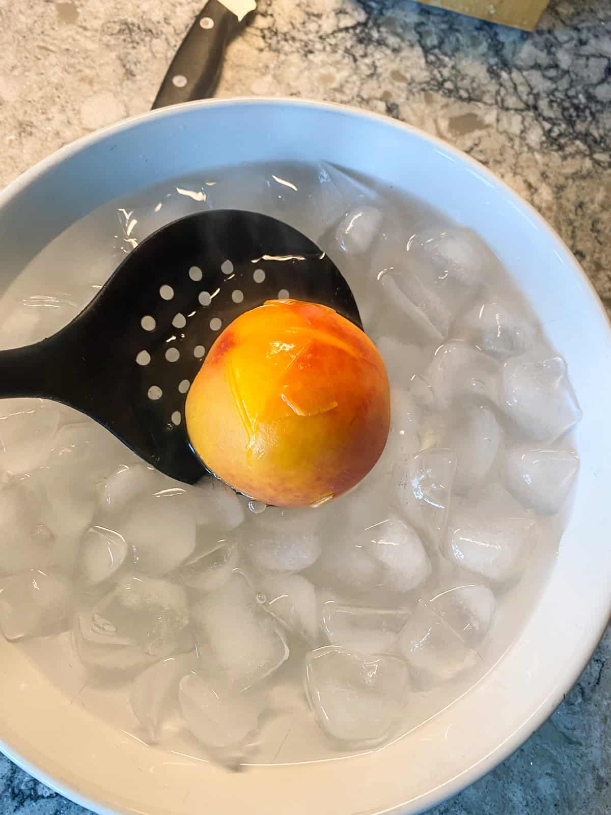 Blanched peach being lowered into an ice bath.