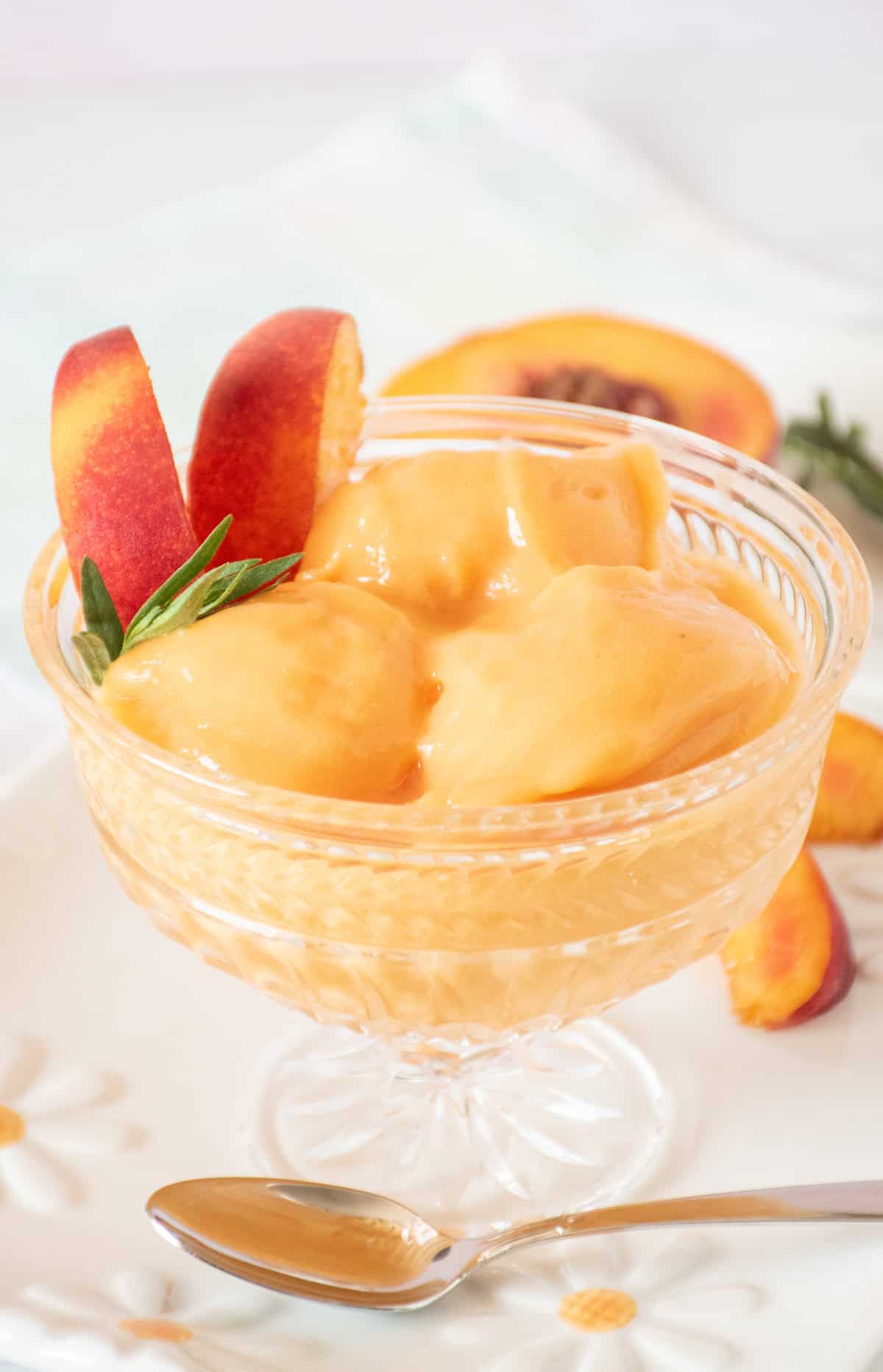 Glass dish with three scoops of peach sorbet; garnished with peach slices and fresh tarragon.