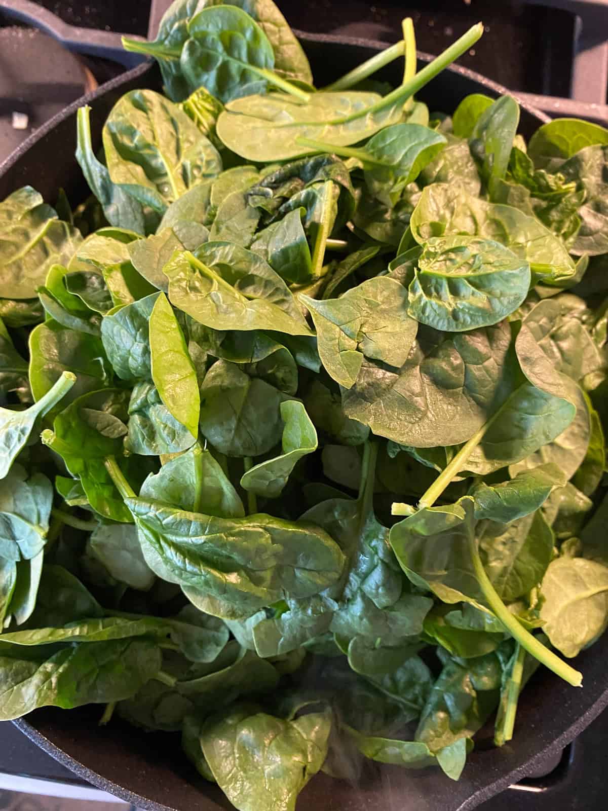 Raw spinach added to the hot pan.
