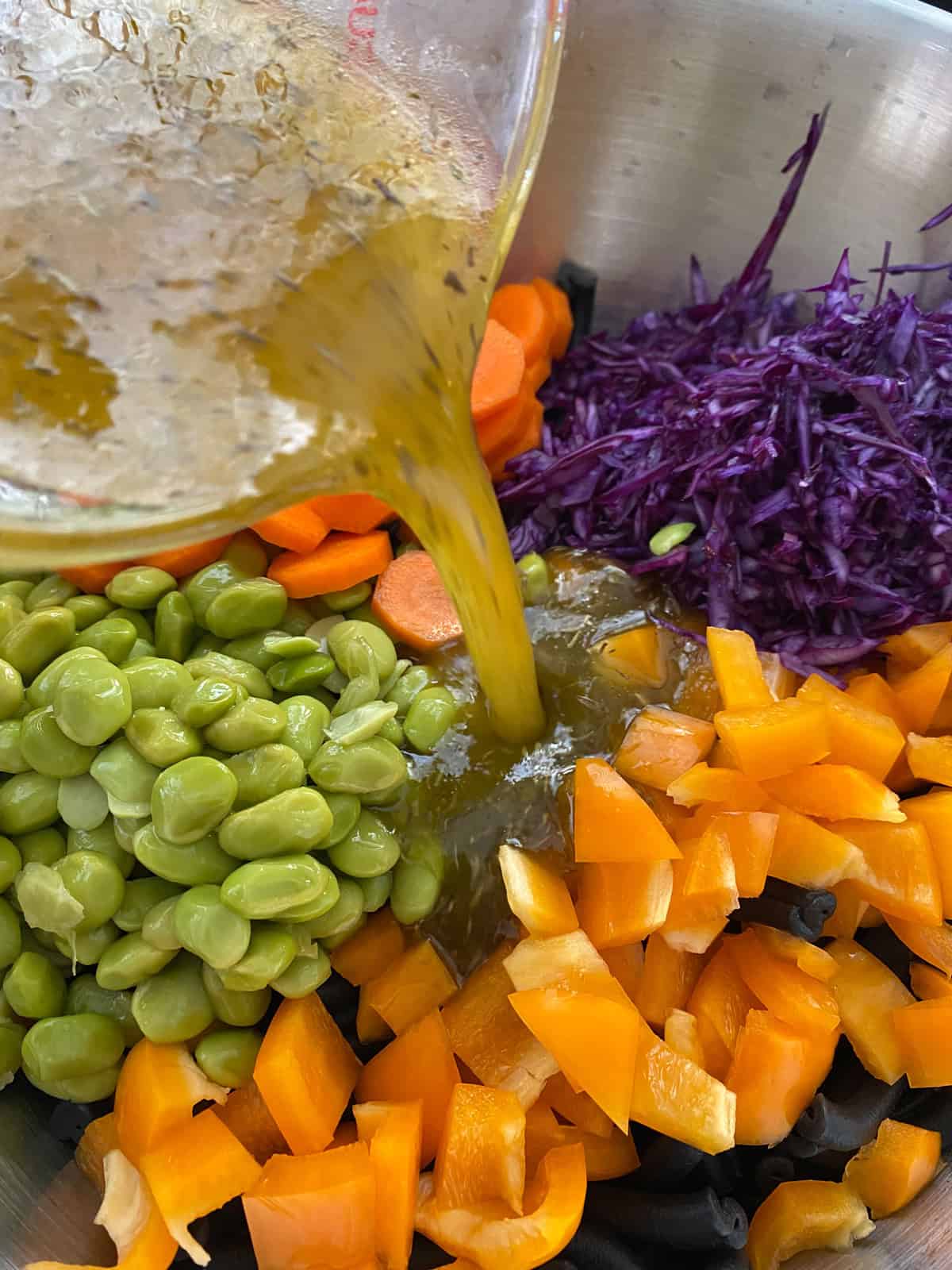Dressing being poured into pasta and vegetables.