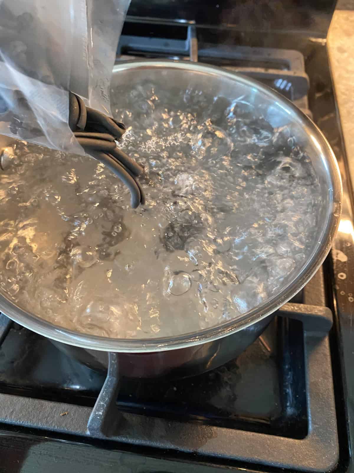 Squid ink pasta being poured into a boiling pot of water.
