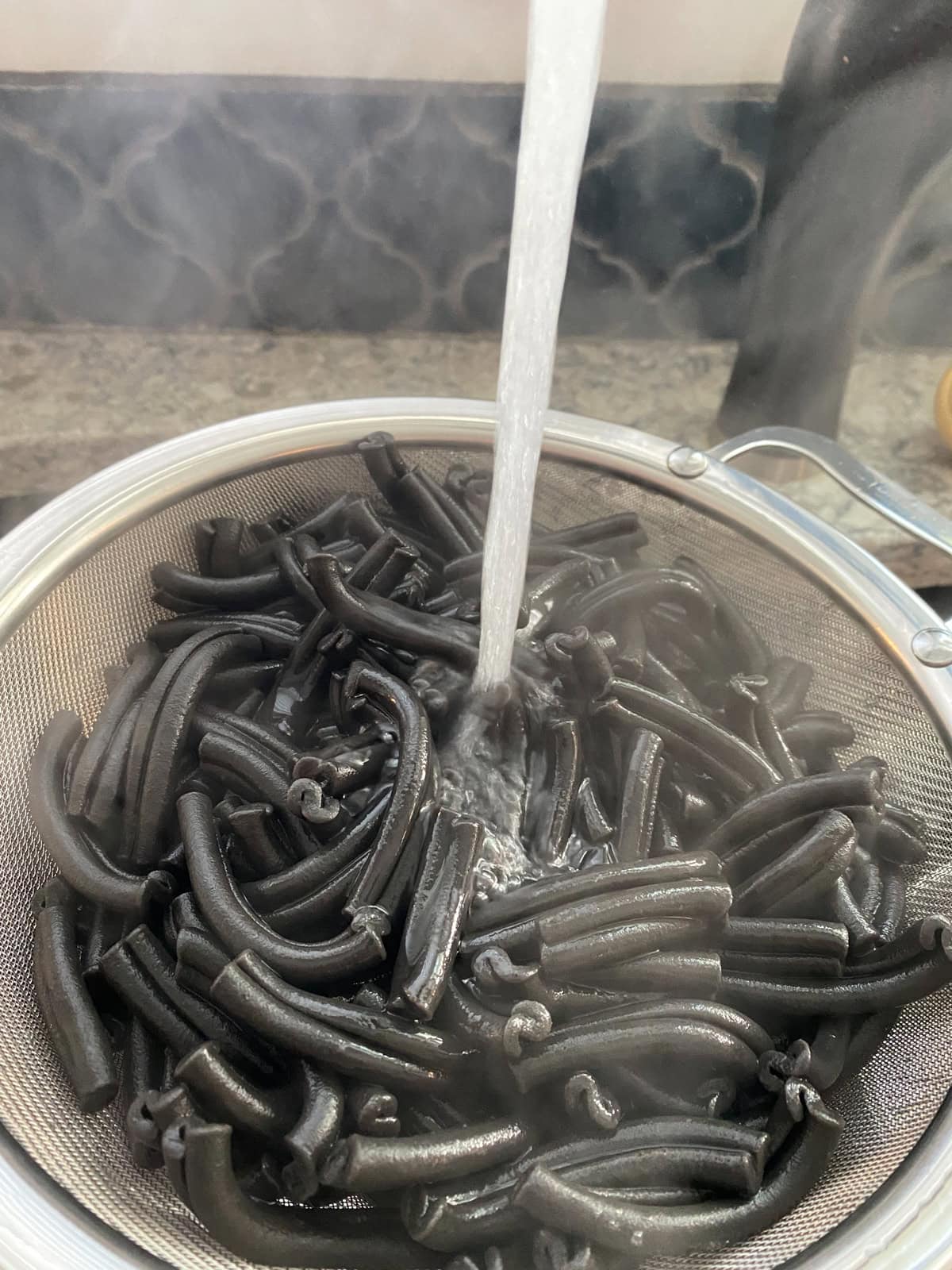 Squid ink pasta in a strainer, with cool running water.