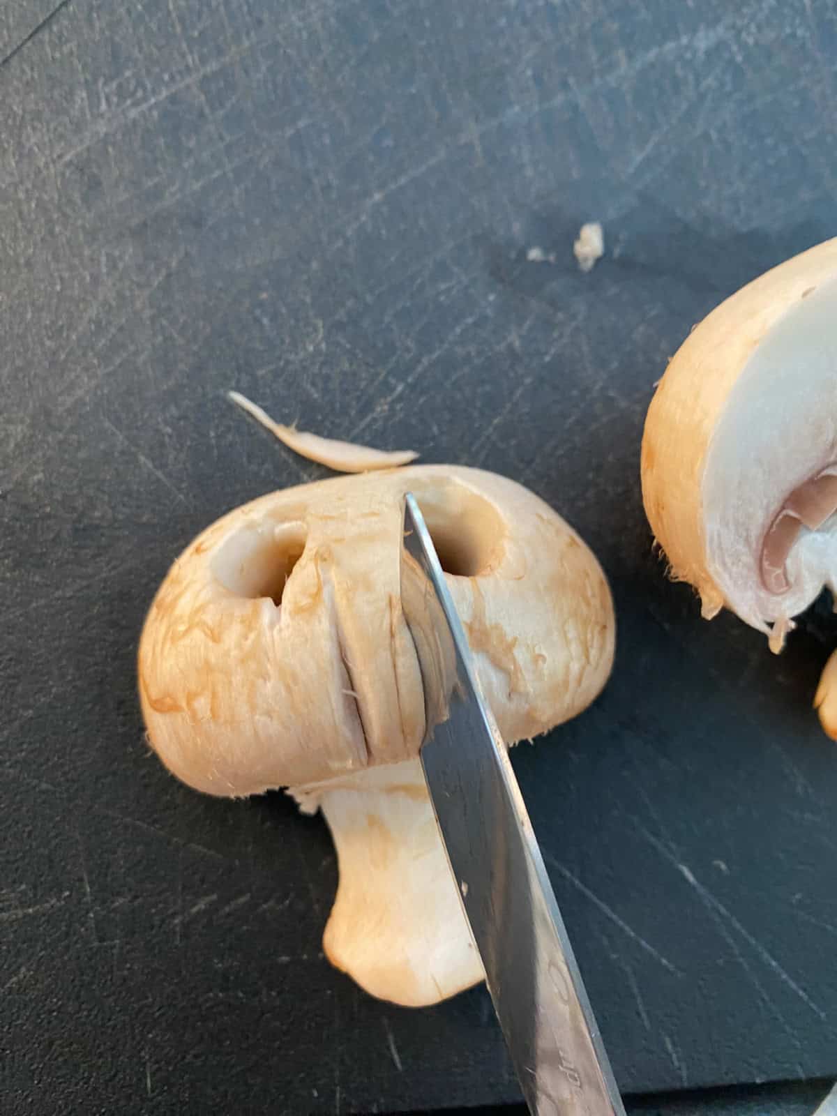 A knife being used to cut nose slits in the mushroom cap.