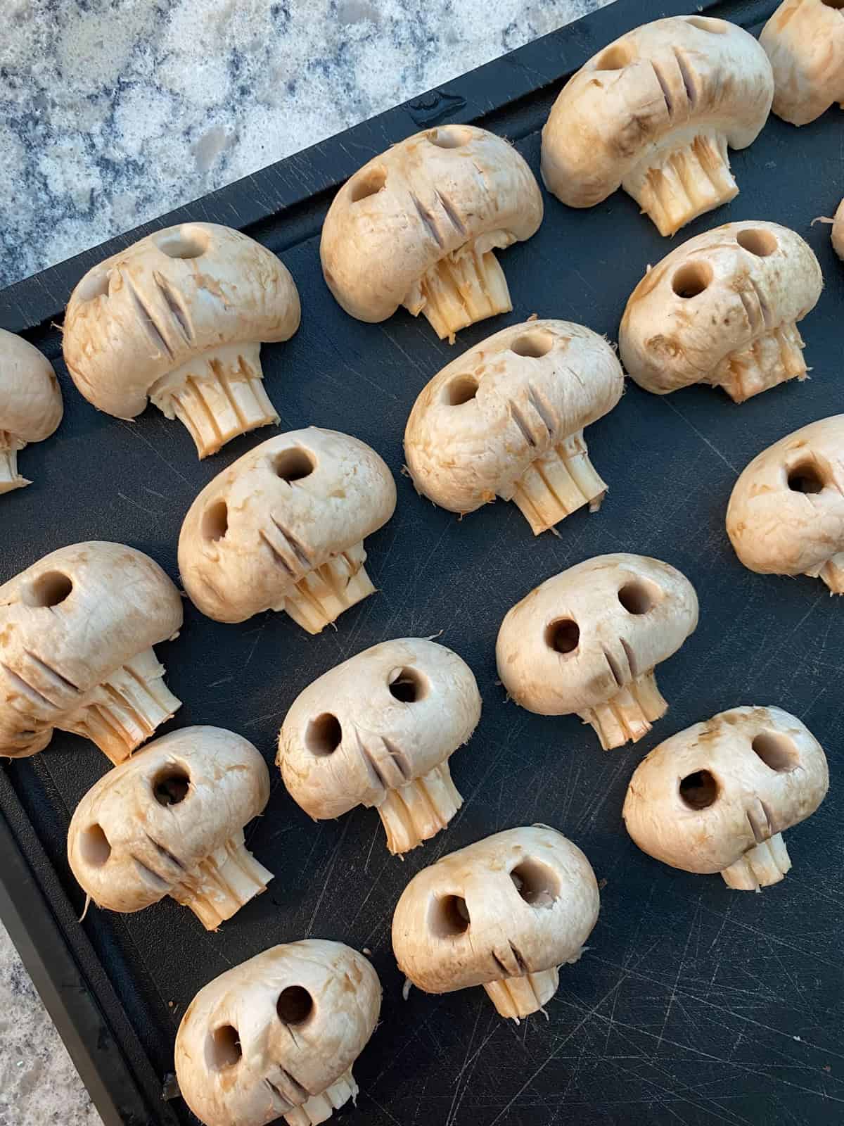 Mushroom halves carved into skulls on a cutting board.