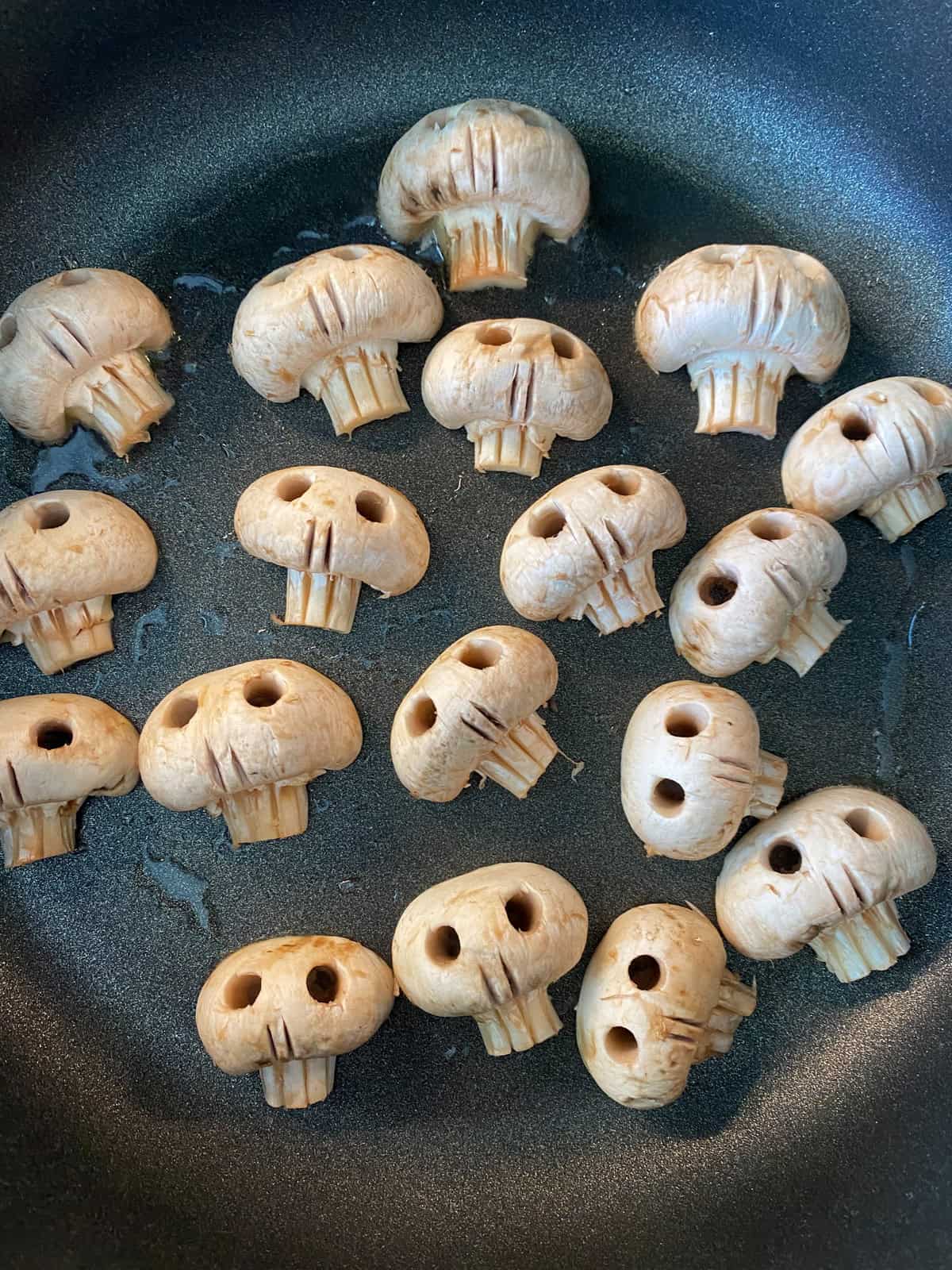 Carved mushroom skulls in a pan sauteing with oil.