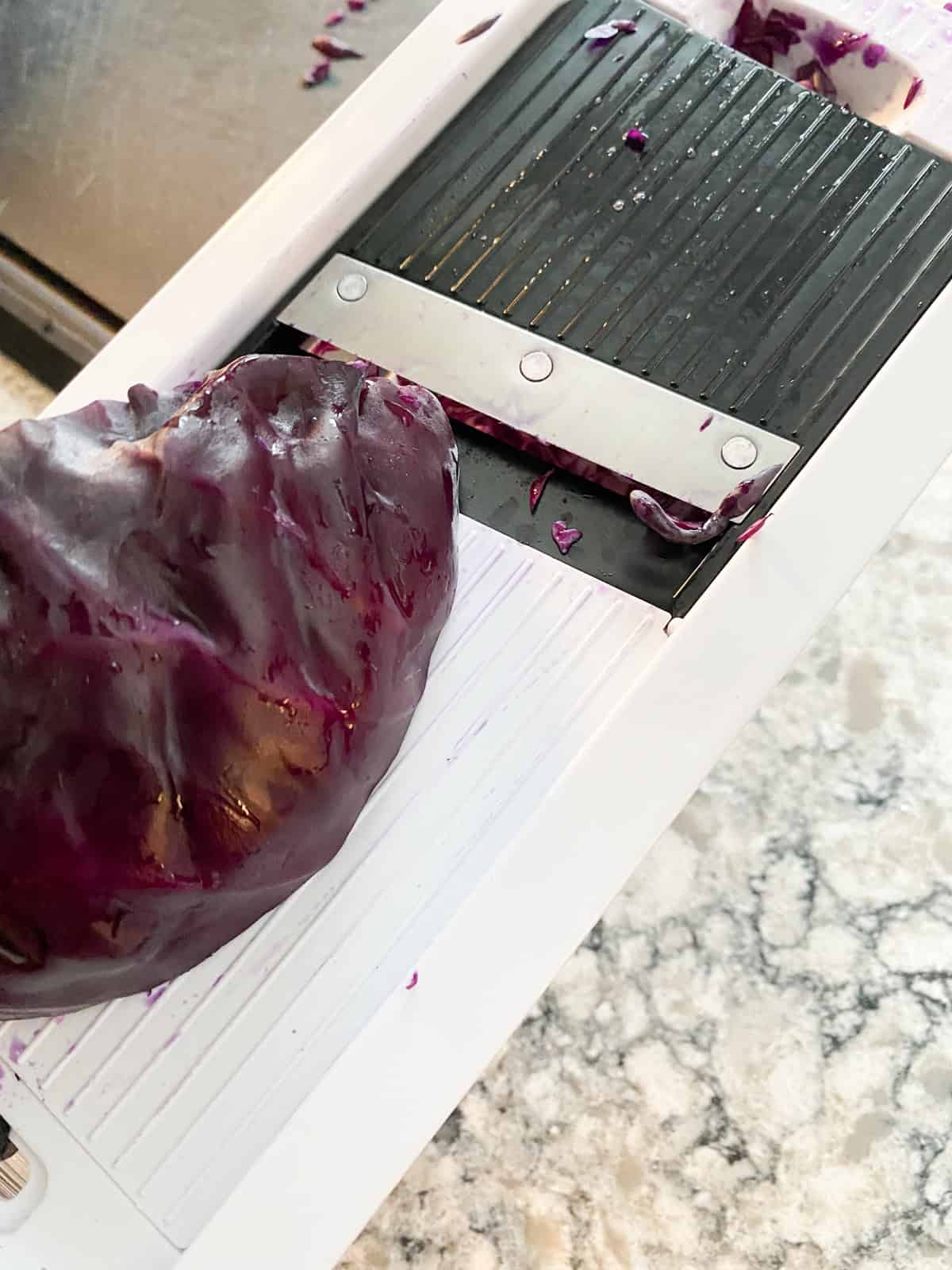 Cabbage being shredded on a mandolin slicer.
