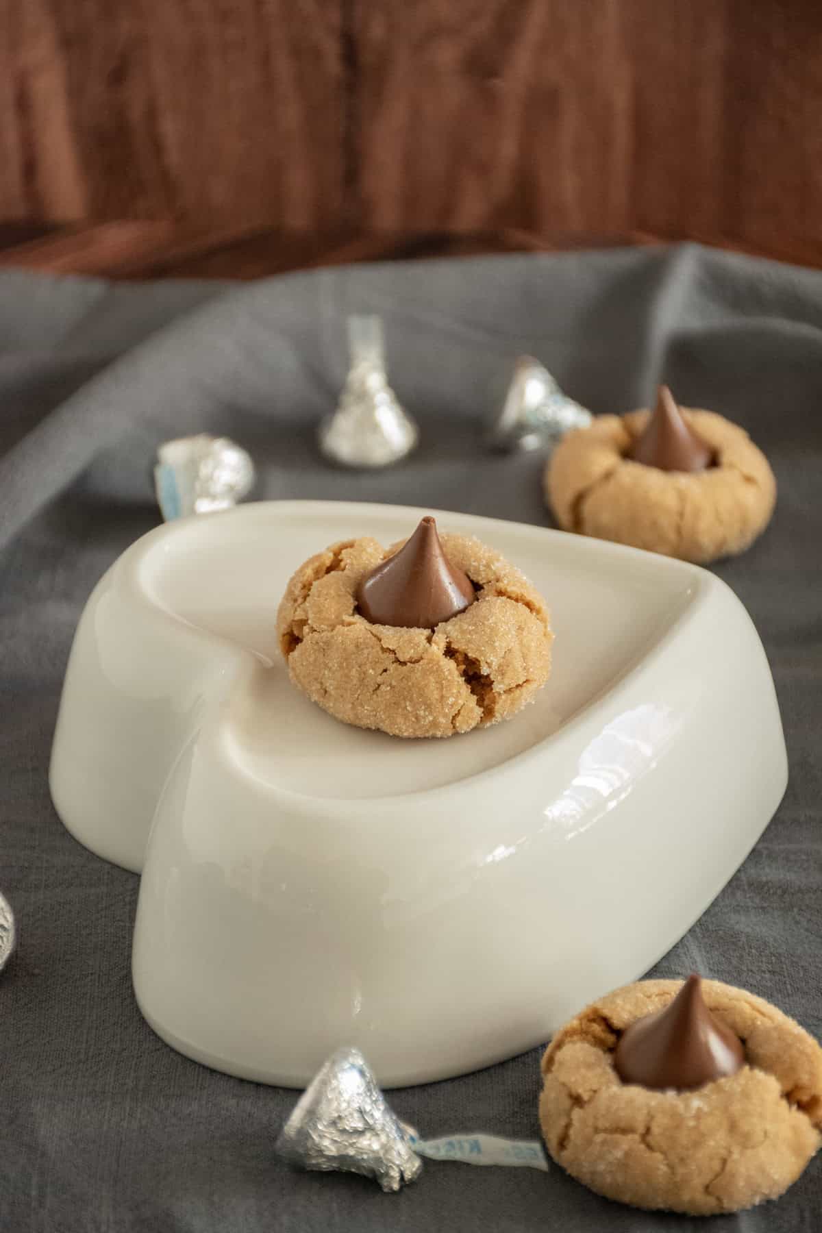 Peanut butter blossom on a heart shaped dish, with more cookies and kisses scattered around the table.