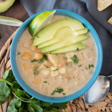 Overhead image of a bowl of white chili, garnished with sliced avocado, a lime wedge, and chopped cilantro.