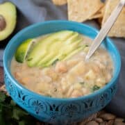 Bowl of white chili, garnished with sliced avocado, a lime wedge, and chopped cilantro.