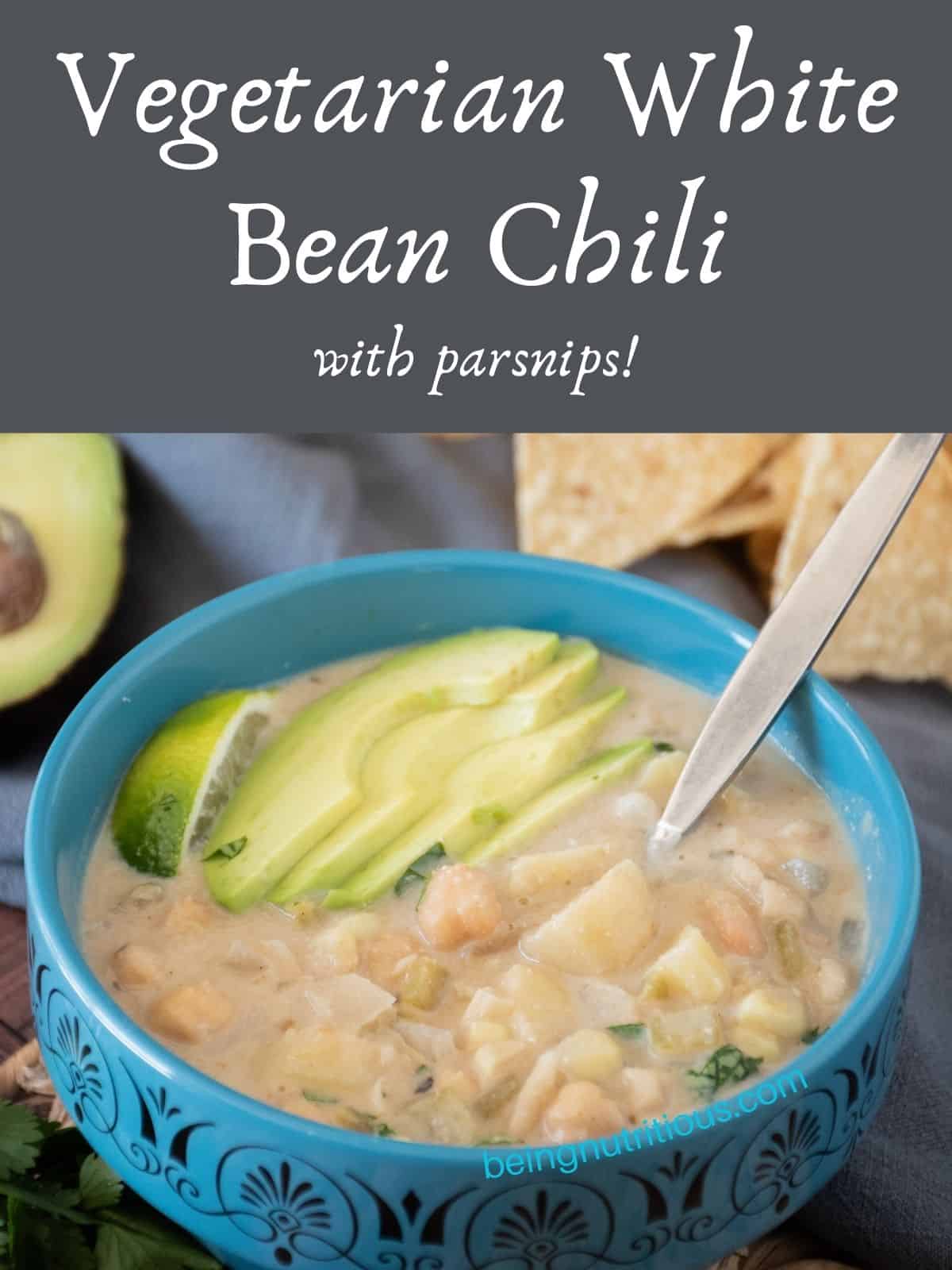 Bowl of white chili, garnished with sliced avocado, a lime wedge, and chopped cilantro. Text overlay: Vegetarian White Bean Chili with parsnips.