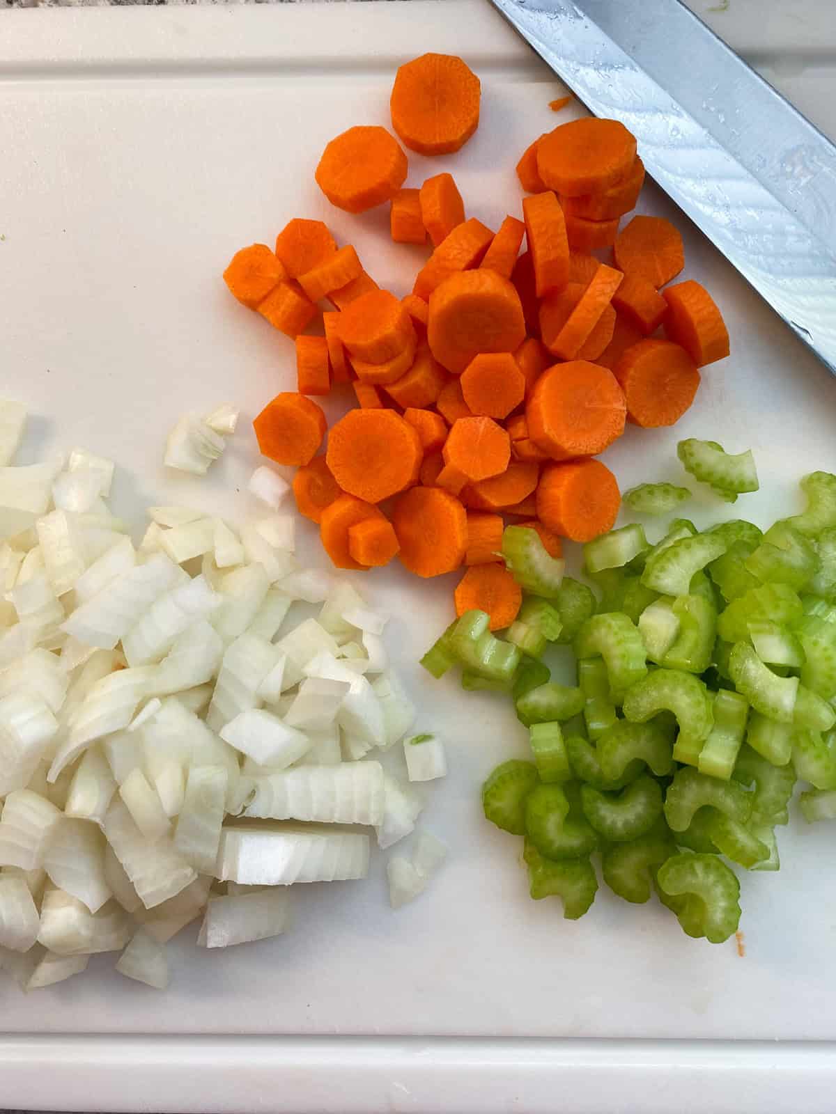 Chopped onions, carrots, and celery, on a cutting board.