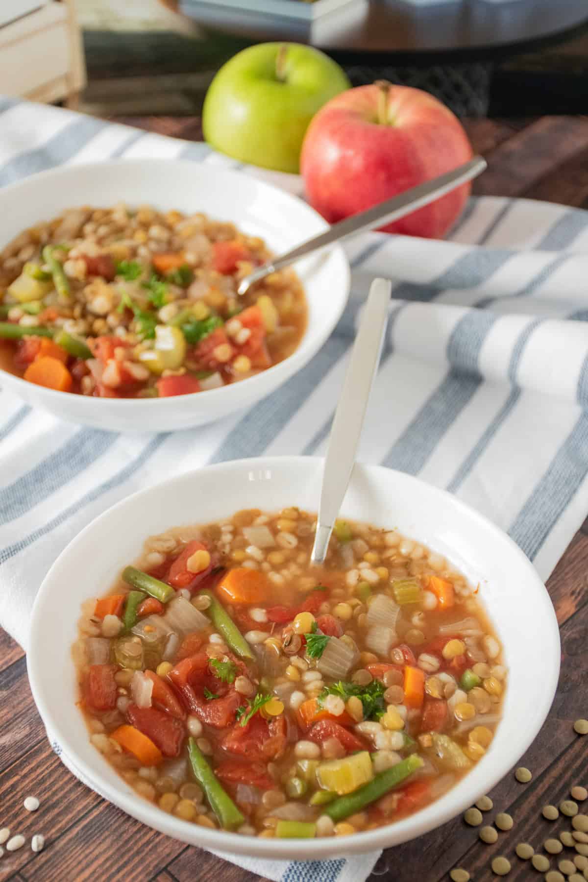 Two bowls of barley lentil soup, with two apples in the background.
