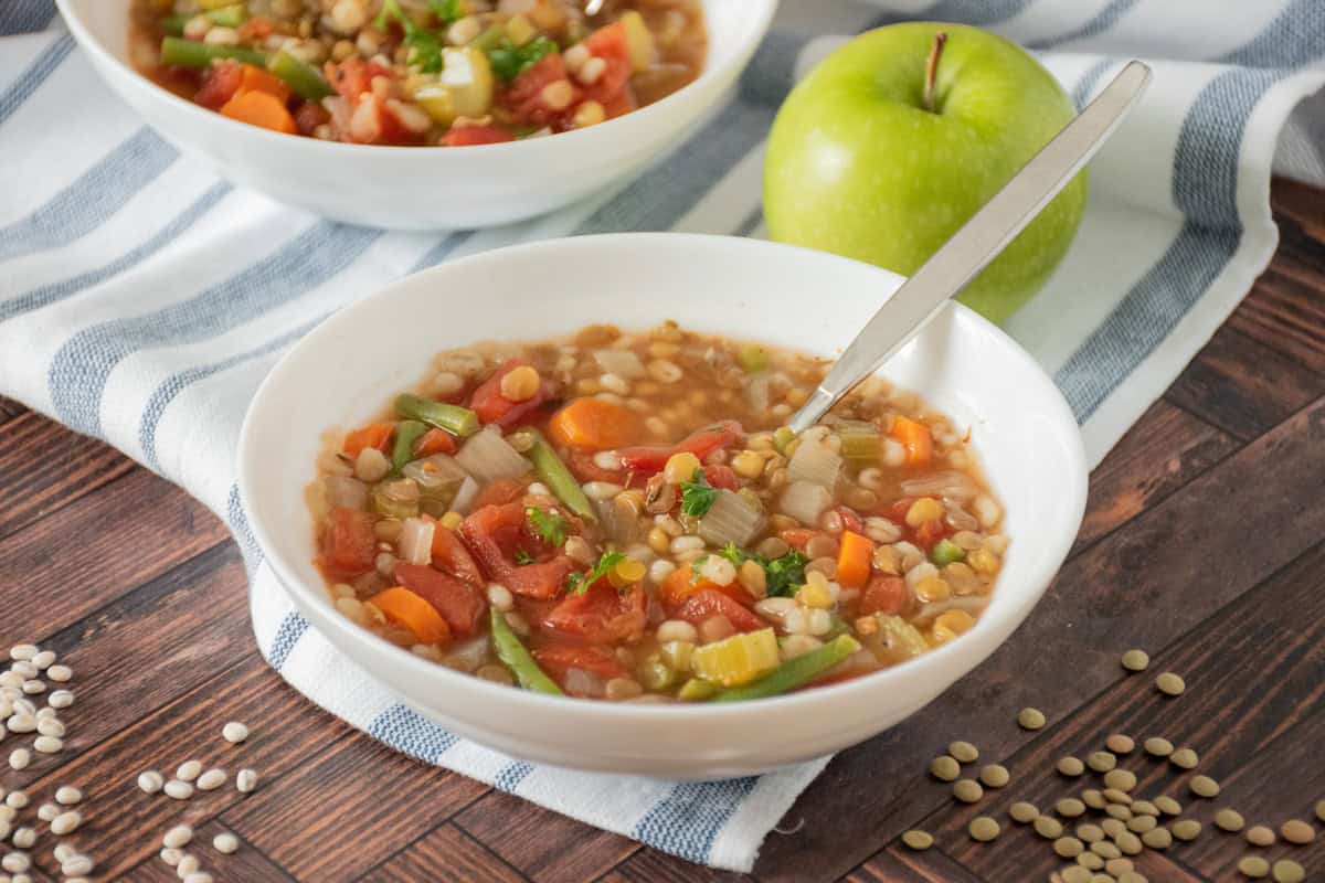 Bowl of soup with a spoon in it, and a green apple on the table behind it.