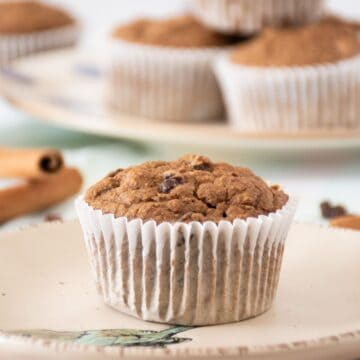 Single muffin on a dish. A stack of muffins is visible in the background.