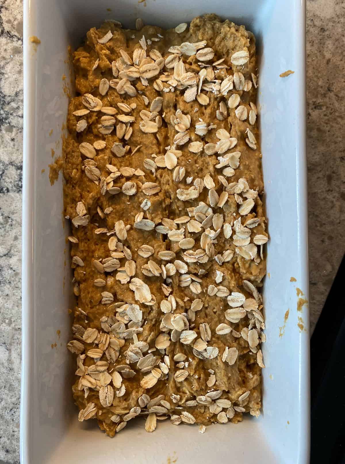 Bread batter, in loaf pan, sprinkled with oats.