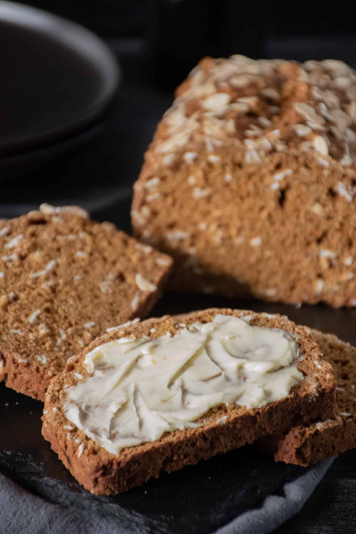 Slice of bread with butter on it. Other slices, and rest of loaf visible in background.