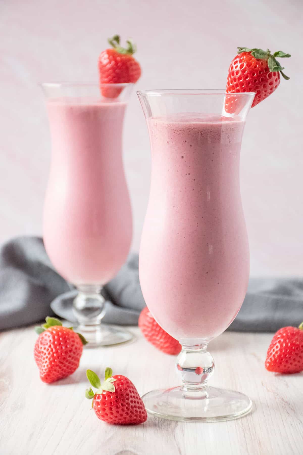Two tall glasses of a smoothie, garnished with a fresh strawberry.