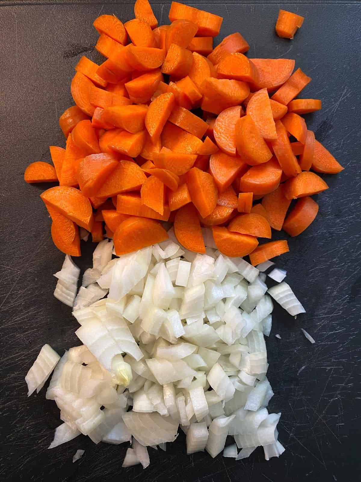 Chopped onions and carrots on a cutting board.