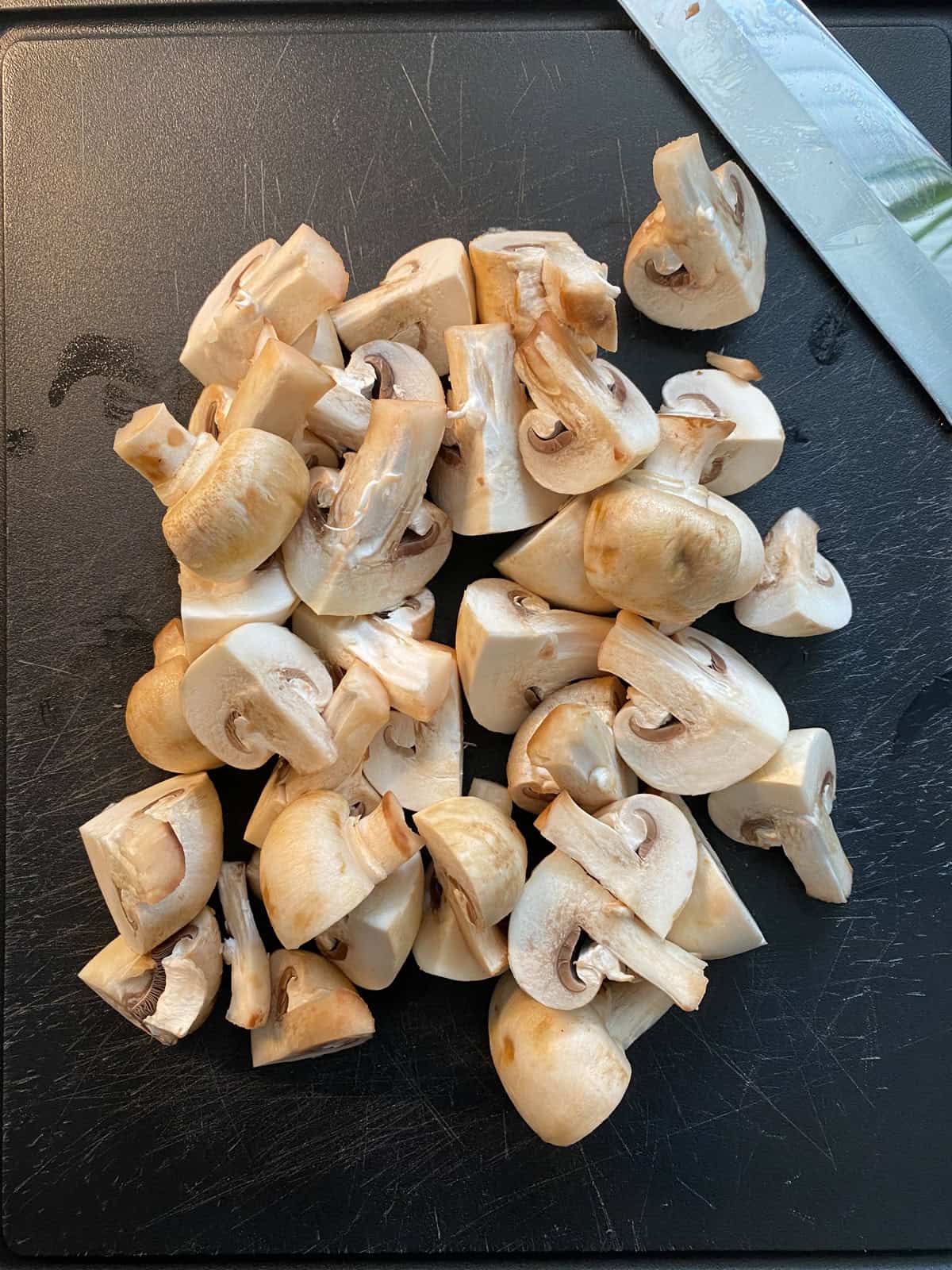 Mushrooms, quartered on a cutting board.