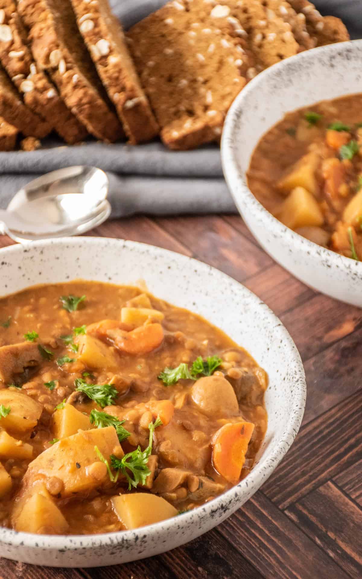 Bowl of lentil and mushroom stew, garnished with parsley. Another bowl, and a sliced loaf of bread visible in the background.