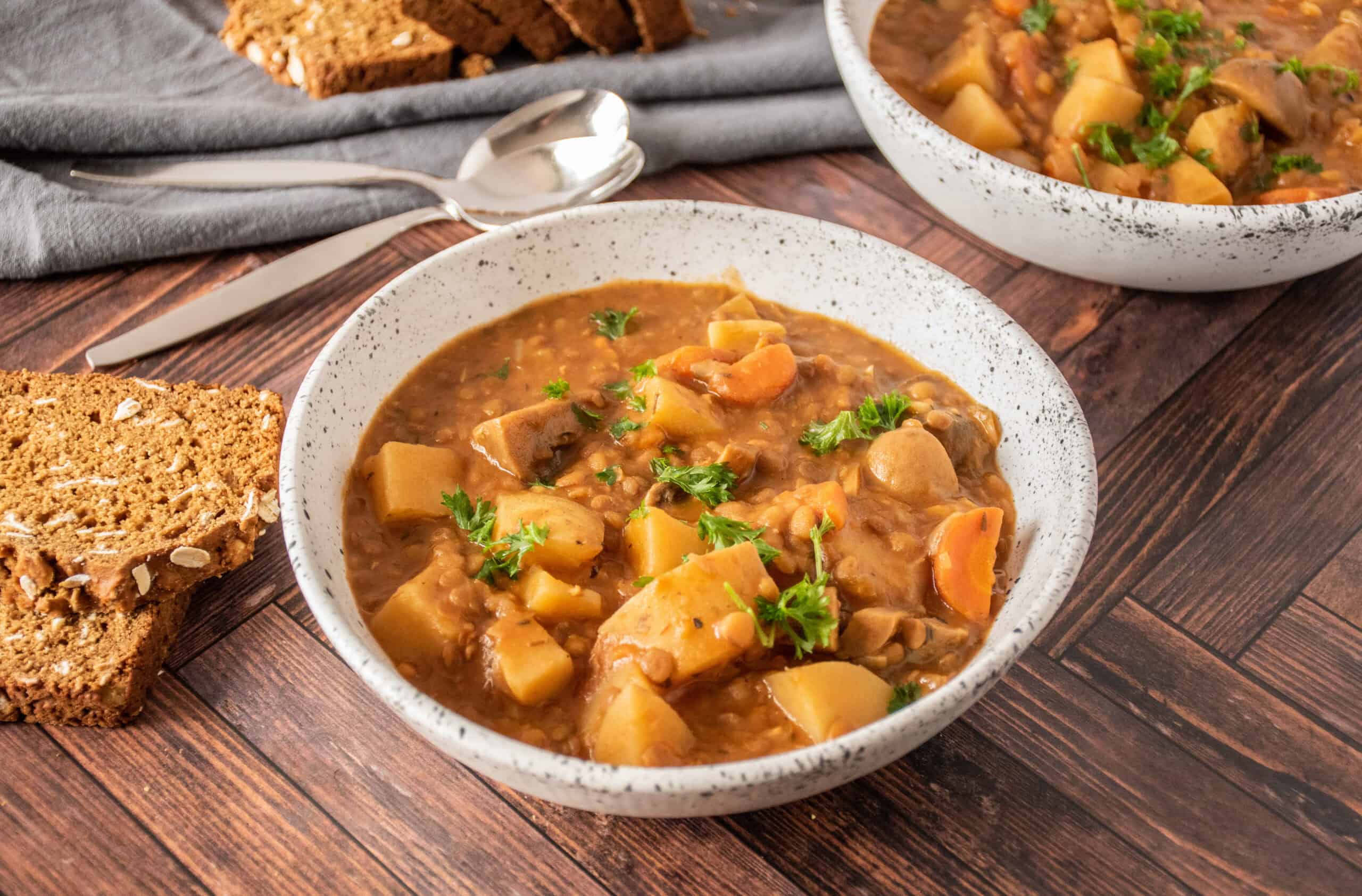 Bowl of lentil and mushroom stew, garnished with parsley, and slices of bread on the side.