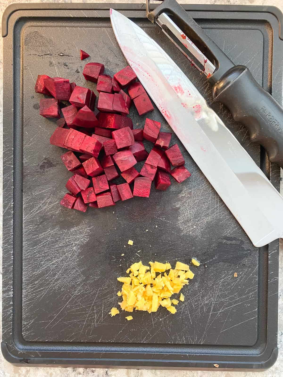 Chopped beet, and diced ginger on a cutting board, with a knife and vegetable peeler.