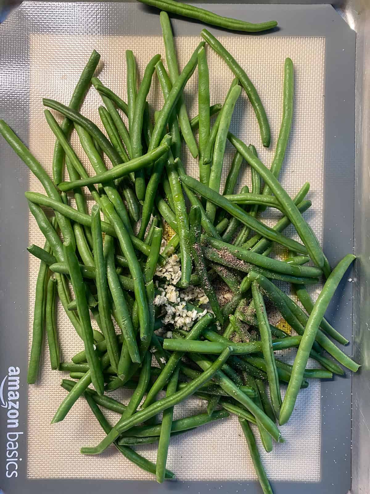 Fresh green beans, oil, garlic, salt, and pepper, on a baking sheet.