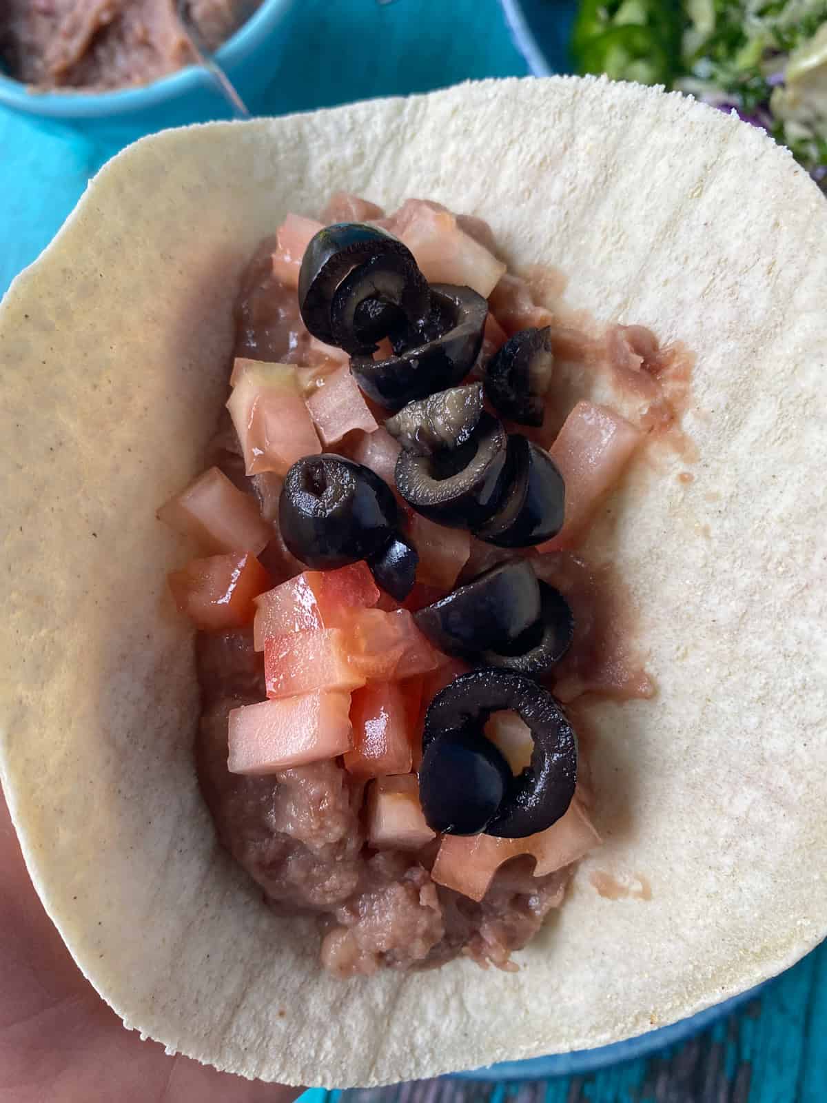 Corn tortilla with refried beans, tomatoes, and olives.