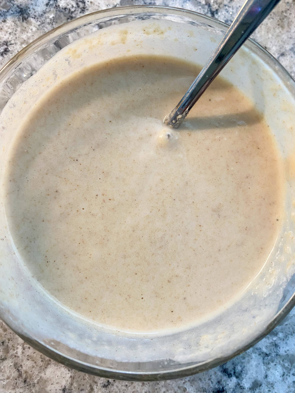 A bowl of tahini dressing with a spoon in it