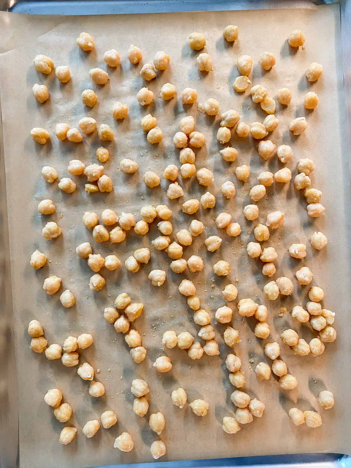 Chickpeas spread on a baking sheet, ready to go in the oven.