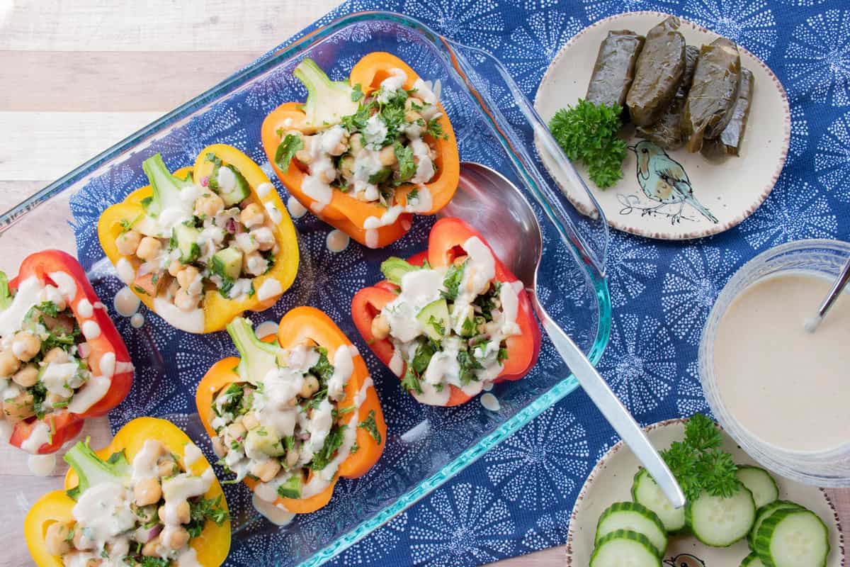 A casserole dish with six stuffed peppers in it, drizzled with tahini dressing.