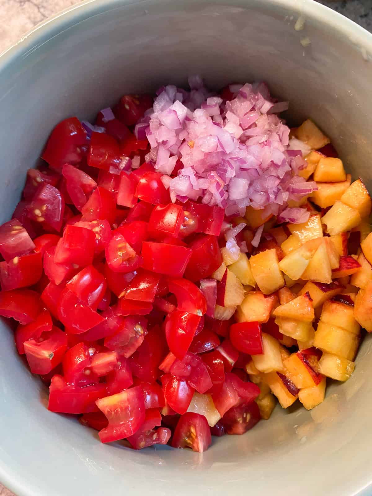 Diced peaches, tomatoes, and red onion in a bowl.