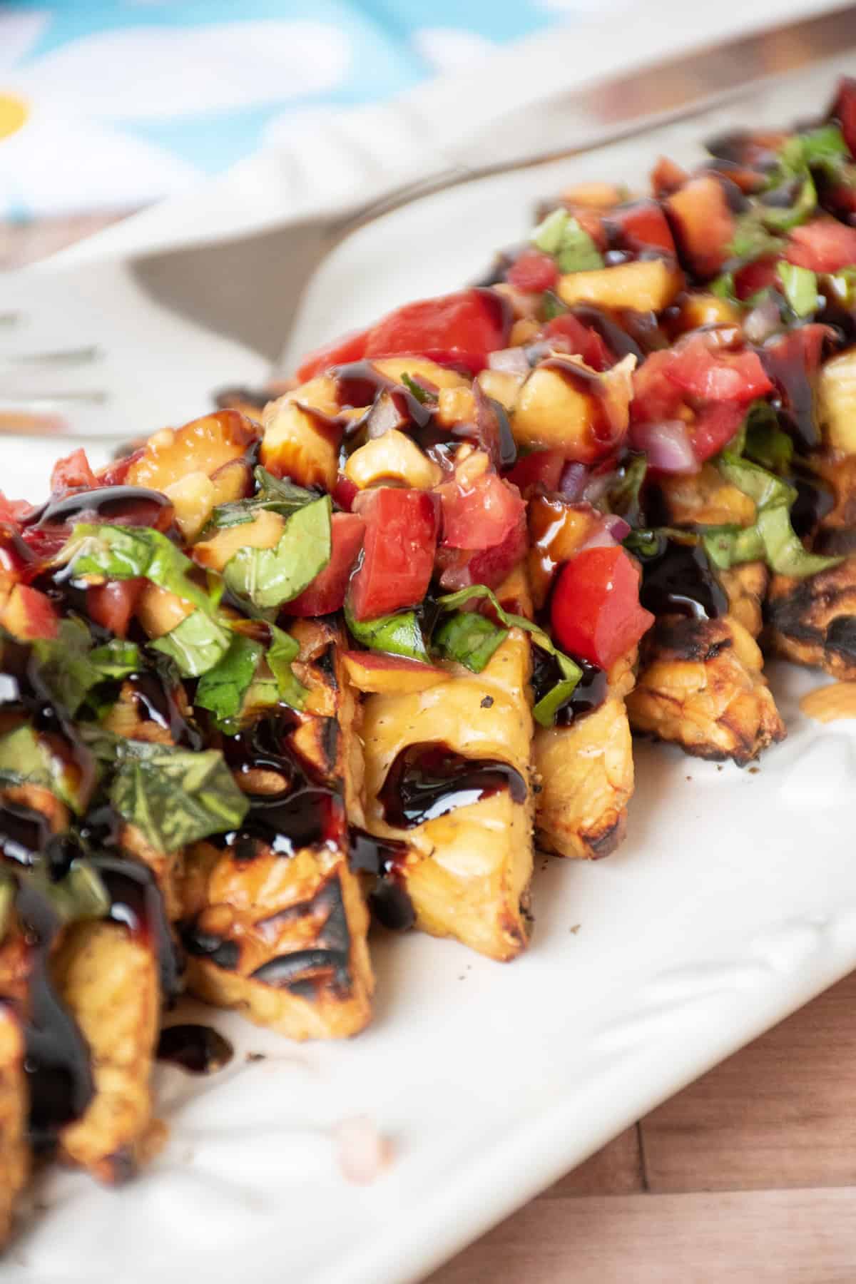 Grilled tempeh triangles in a line on a plate, topped with peach relish and drizzled with balsamic glaze.