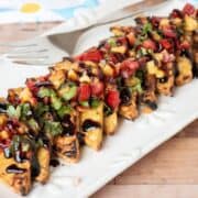 Grilled tempeh triangles in a line on a plate, topped with peach relish and drizzled with balsamic glaze.