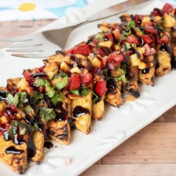 Grilled tempeh triangles in a line on a plate, topped with peach relish and drizzled with balsamic glaze.