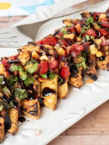 Grilled tempeh triangles in a line on a plate, topped with peach relish and drizzled with balsamic glaze.