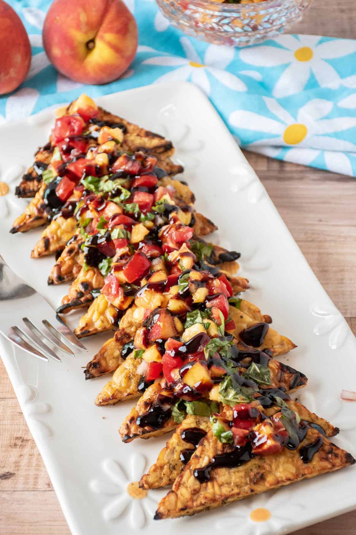 Grilled tempeh triangles in a line on a plate, topped with peach relish and drizzled with balsamic glaze.