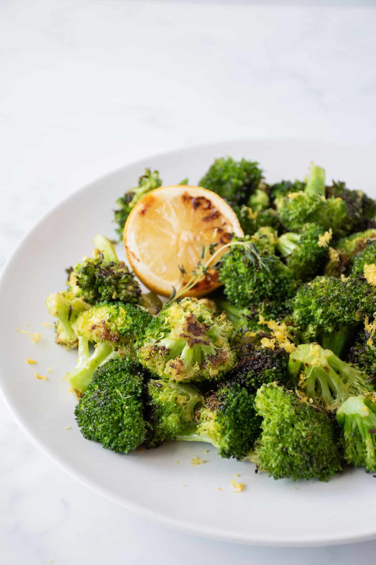 Grilled broccoli on a serving plate, garnished with lemon zest and a stem of thyme.