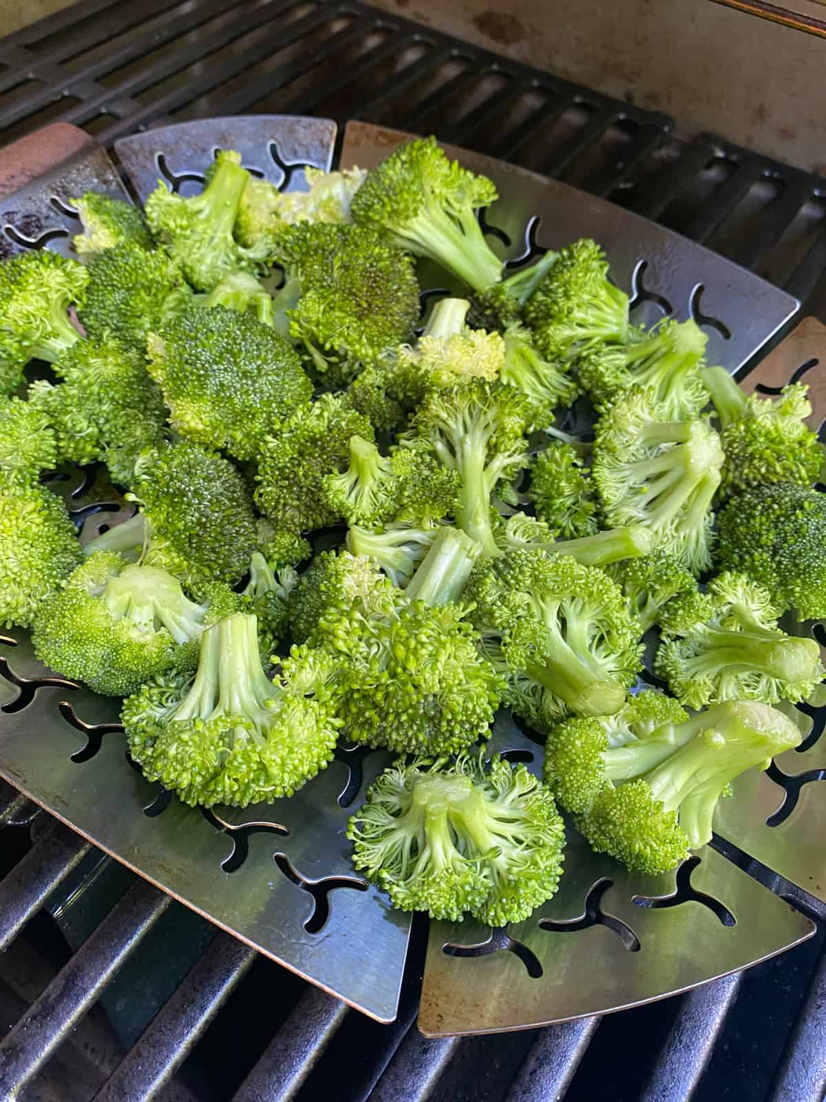 Raw broccoli florets in a grill pan, on the grill.