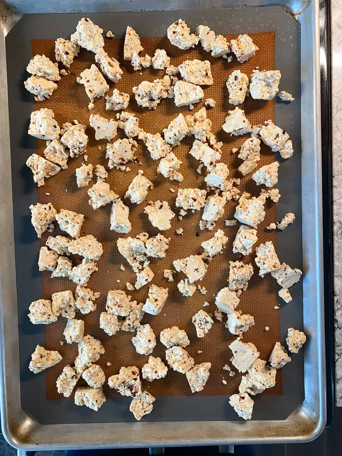 Torn tofu spread on baking sheet, ready for baking.