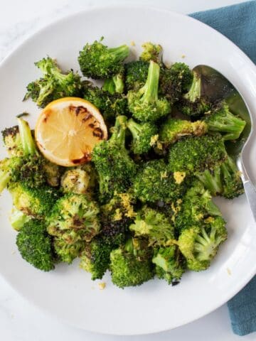 Grilled broccoli on a serving plate, garnished with a grilled lemon half, lemon zest and a stem of thyme.