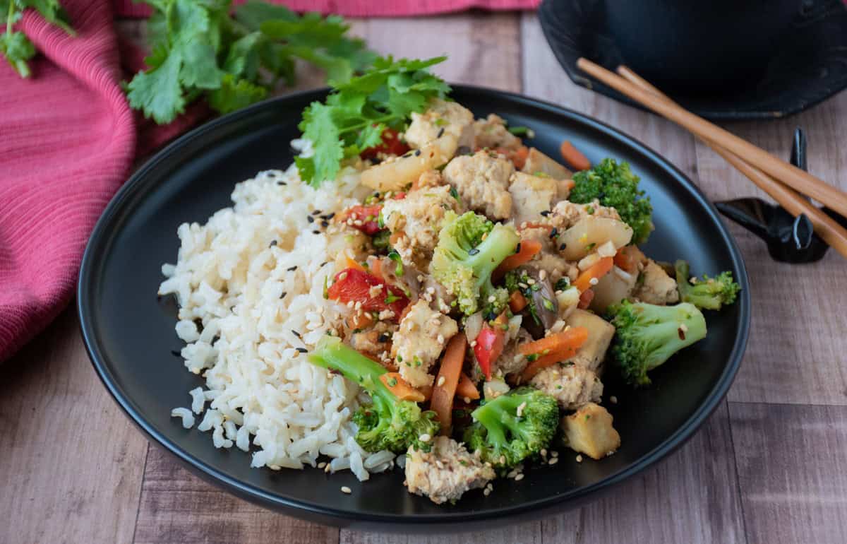 Stir fry on a plate, over brown rice, garnished with sesame seeds and cilantro.